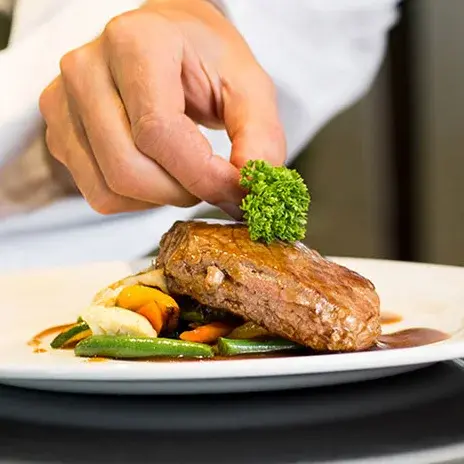 Belmont Gardens Chef Created Meals, chef garnishing a plate.